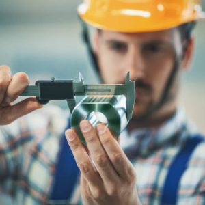 Closeup of metal processing plant worker inspecting certain pieces of finished products. He's making sure that the steel cylinder has proper dimensions. He's using manual caliper device.
